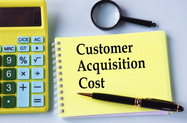 part of a calculator and a pad with words customer acquisition cost and pen and magnifying glass